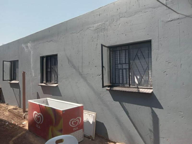 Rear exterior view of the property featuring plastered masonry walls and windows fitted with security bars.