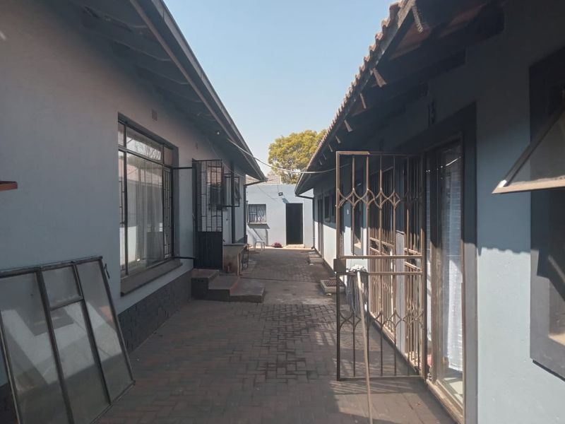 A narrow paved exterior walkway between two residential building wings, featuring security gates and metal window frames.