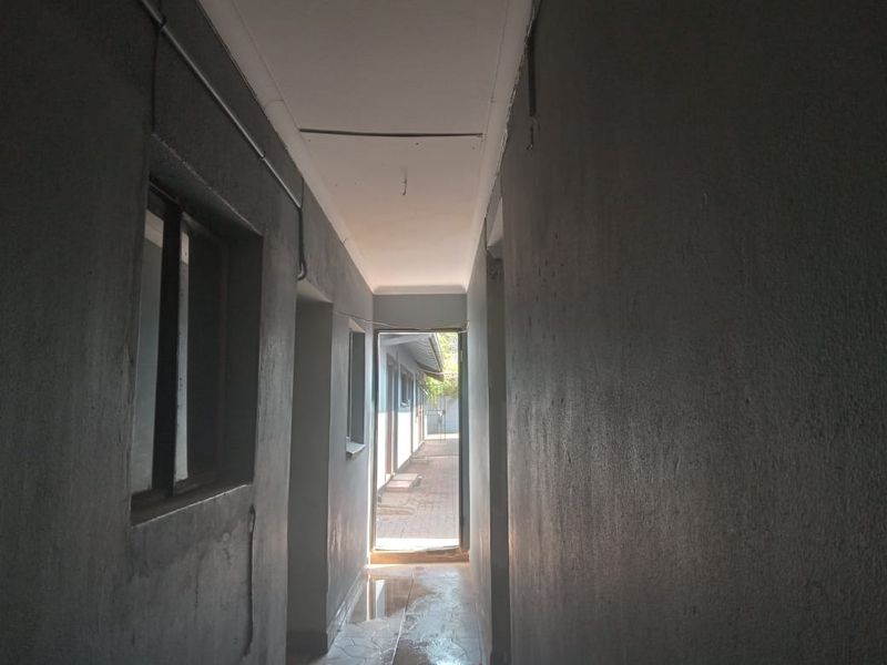 A narrow, unfinished hallway with exposed electrical conduit and tiled flooring, leading to an exterior doorway.