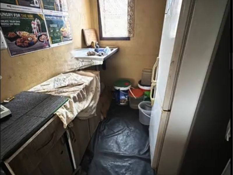 A small scullery or utility area featuring a wall-mounted sink, built-in cabinetry, and a window, currently in need of significant renovation and repair.