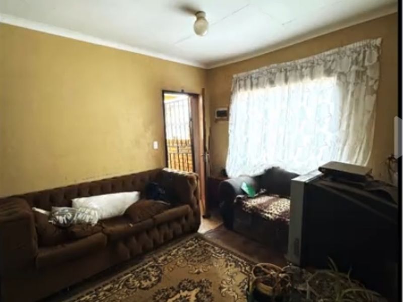 A living room area featuring basic finishes, including a security gate at the entrance and visible wear on the walls and ceiling.