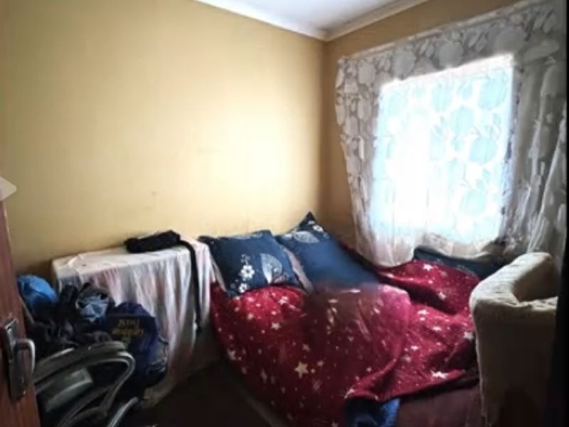 A compact bedroom featuring a window with natural light, requiring cosmetic updates to the walls and ceiling to improve its overall condition.