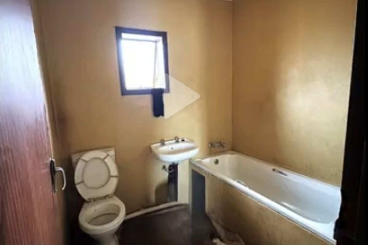 A dated bathroom featuring a standard bathtub, wall-mounted basin, and toilet, requiring significant renovation and cosmetic updates to improve its condition.