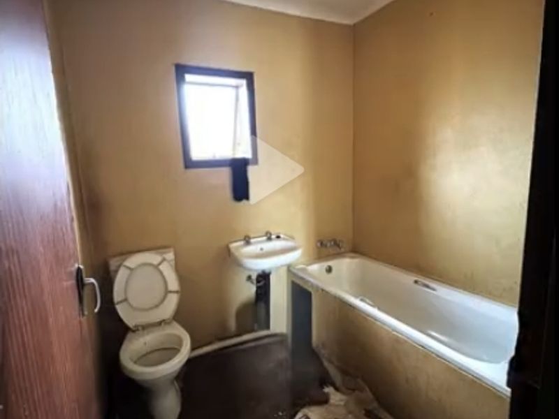A dated bathroom featuring a standard bathtub, wall-mounted basin, and toilet, requiring significant renovation and cosmetic updates to improve its condition.