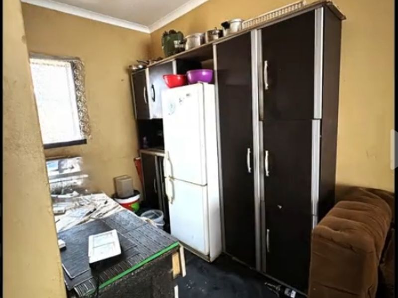 A compact kitchen area featuring built-in cabinetry and basic lighting, currently requiring significant cosmetic updates and maintenance to improve its overall condition.