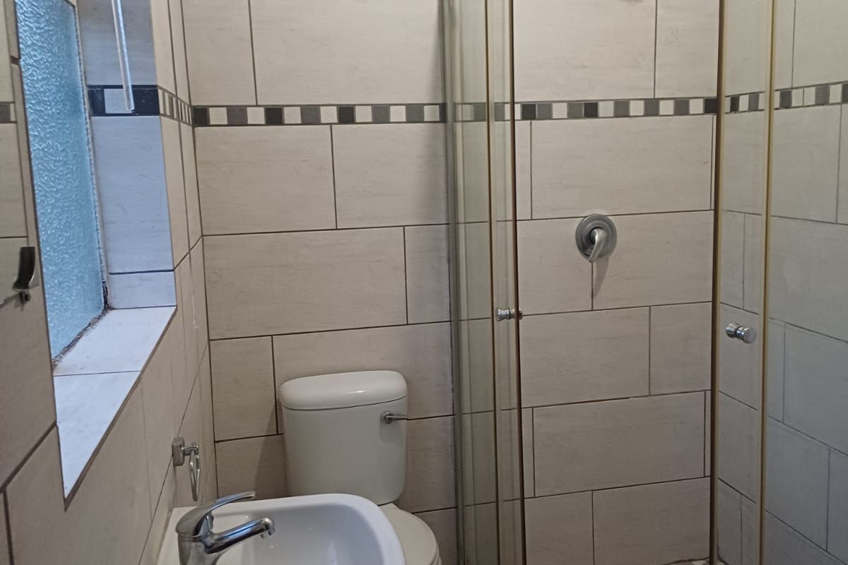 A clean, modern bathroom featuring a glass-enclosed shower with pebble flooring, a pedestal basin, and neutral wall tiling.
