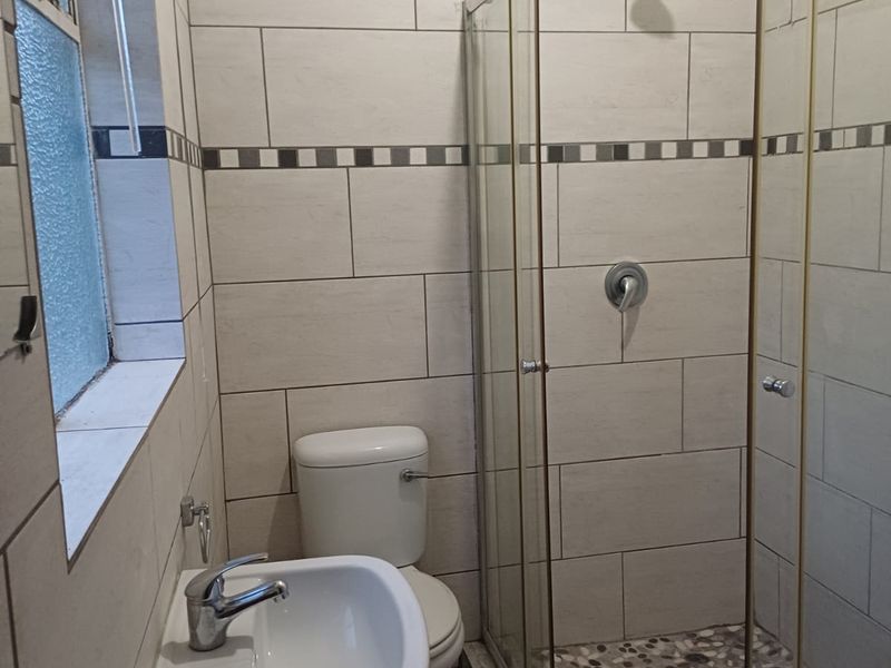 A clean, modern bathroom featuring a glass-enclosed shower with pebble flooring, a pedestal basin, and neutral wall tiling.