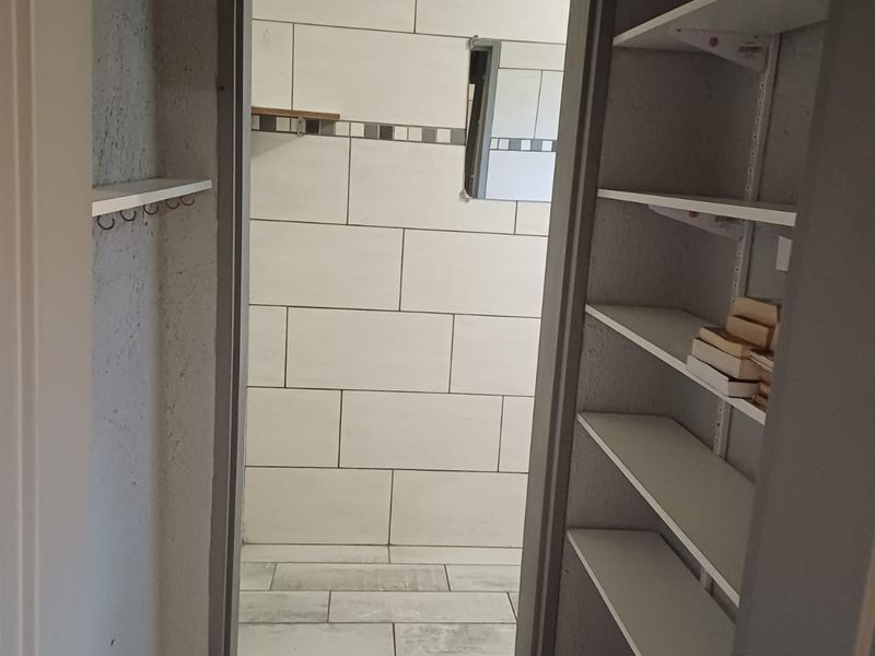 A functional scullery or pantry area featuring built-in shelving, tiled flooring, and tiled wall finishes, currently in need of minor cosmetic completion.