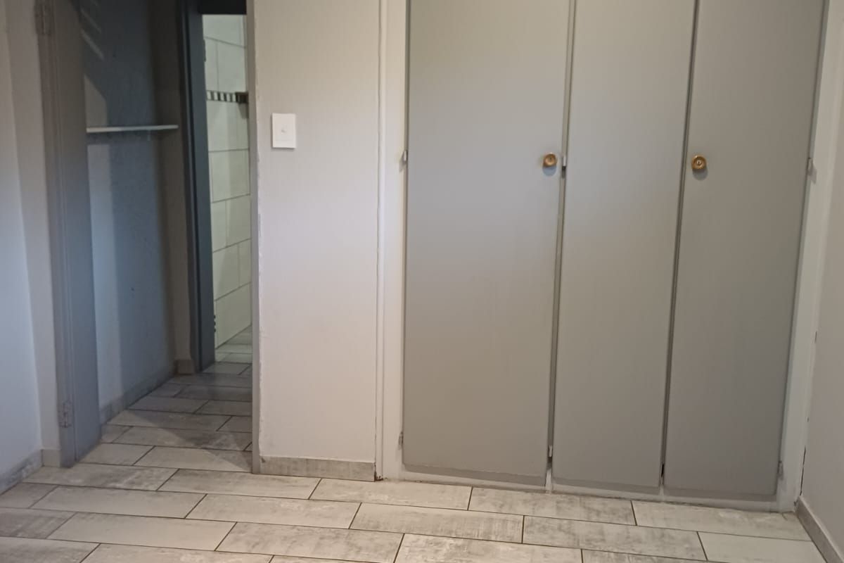 A vacant bedroom featuring modern wood-look floor tiles, built-in cupboards, and an adjacent doorway leading to a tiled bathroom area.
