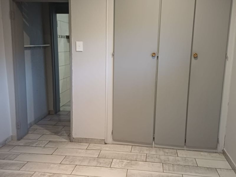 A vacant bedroom featuring modern wood-look floor tiles, built-in cupboards, and an adjacent doorway leading to a tiled bathroom area.