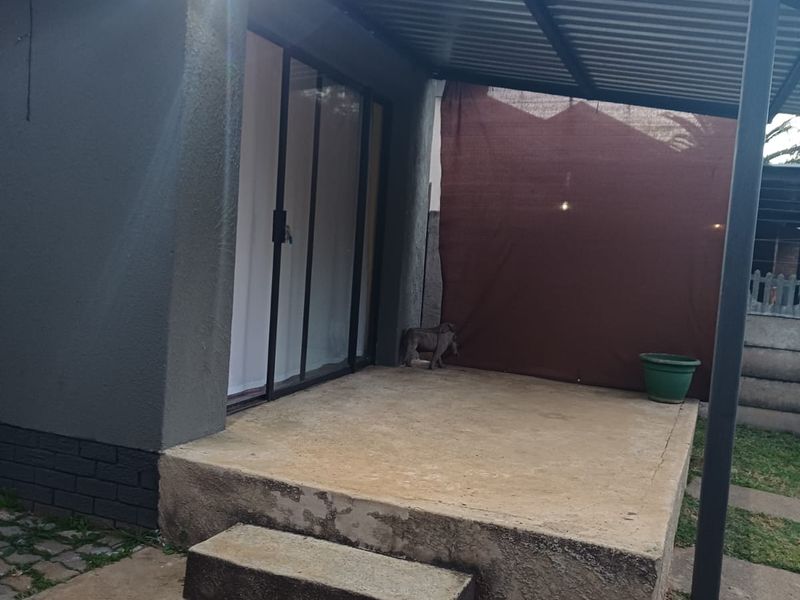 A covered outdoor patio area featuring a concrete slab, metal roofing, and sliding glass door access to the cottage interior.