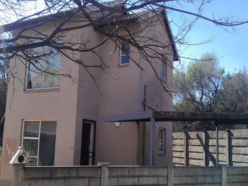 Exterior view of a two-story apartment building featuring a carport, security gate, and perimeter wall, showing signs of exterior wear.