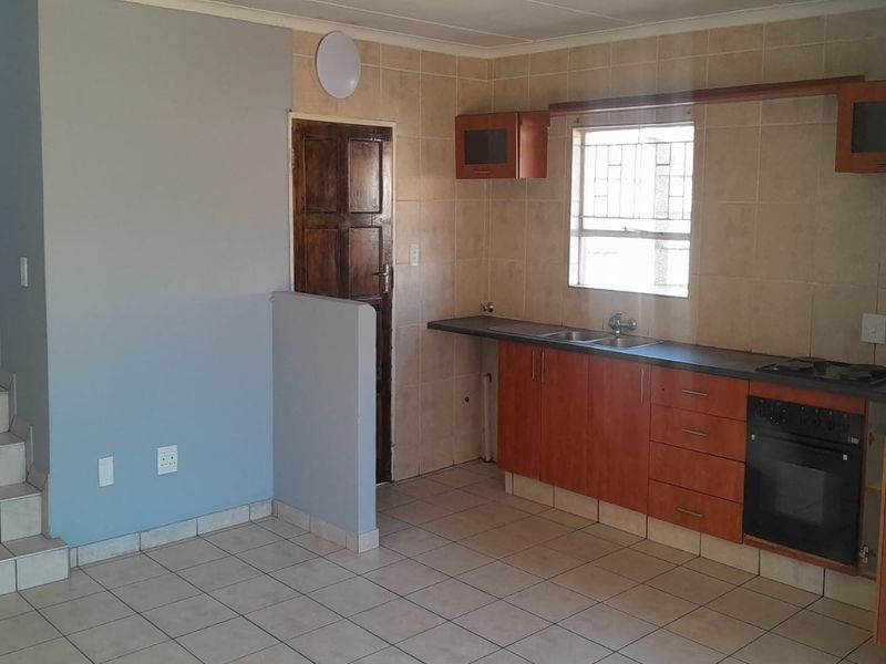 Open-plan kitchen area featuring built-in cabinetry, integrated oven and hob, tiled splashback, and an adjacent staircase with tiled steps.