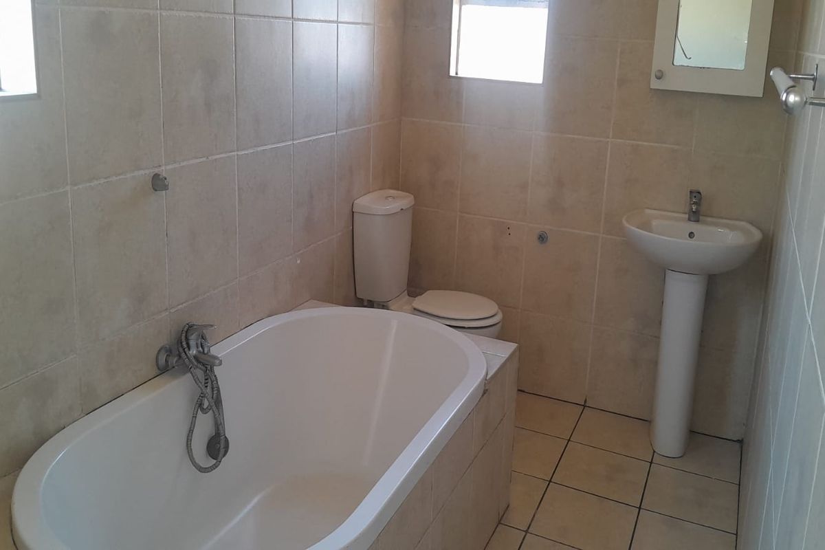 A functional bathroom featuring a pedestal basin, bathtub, and toilet with neutral wall and floor tiling, ready for cosmetic updates.