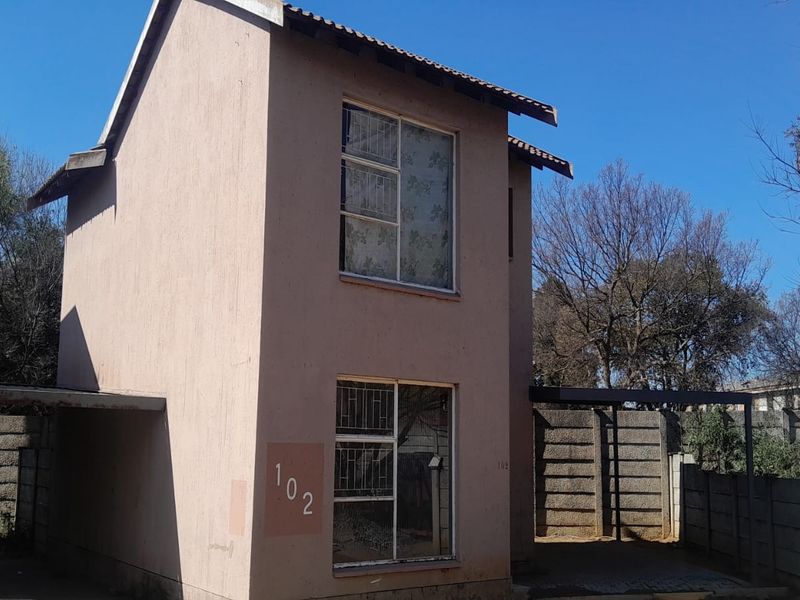 A two-story apartment unit featuring a plastered facade, tiled roof, and an attached carport, enclosed by a precast concrete boundary wall.