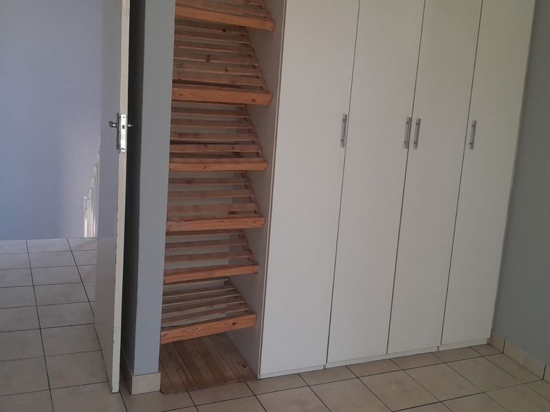 A bedroom featuring built-in cupboards with white doors and an integrated open wooden shelving unit, finished with neutral floor tiles.