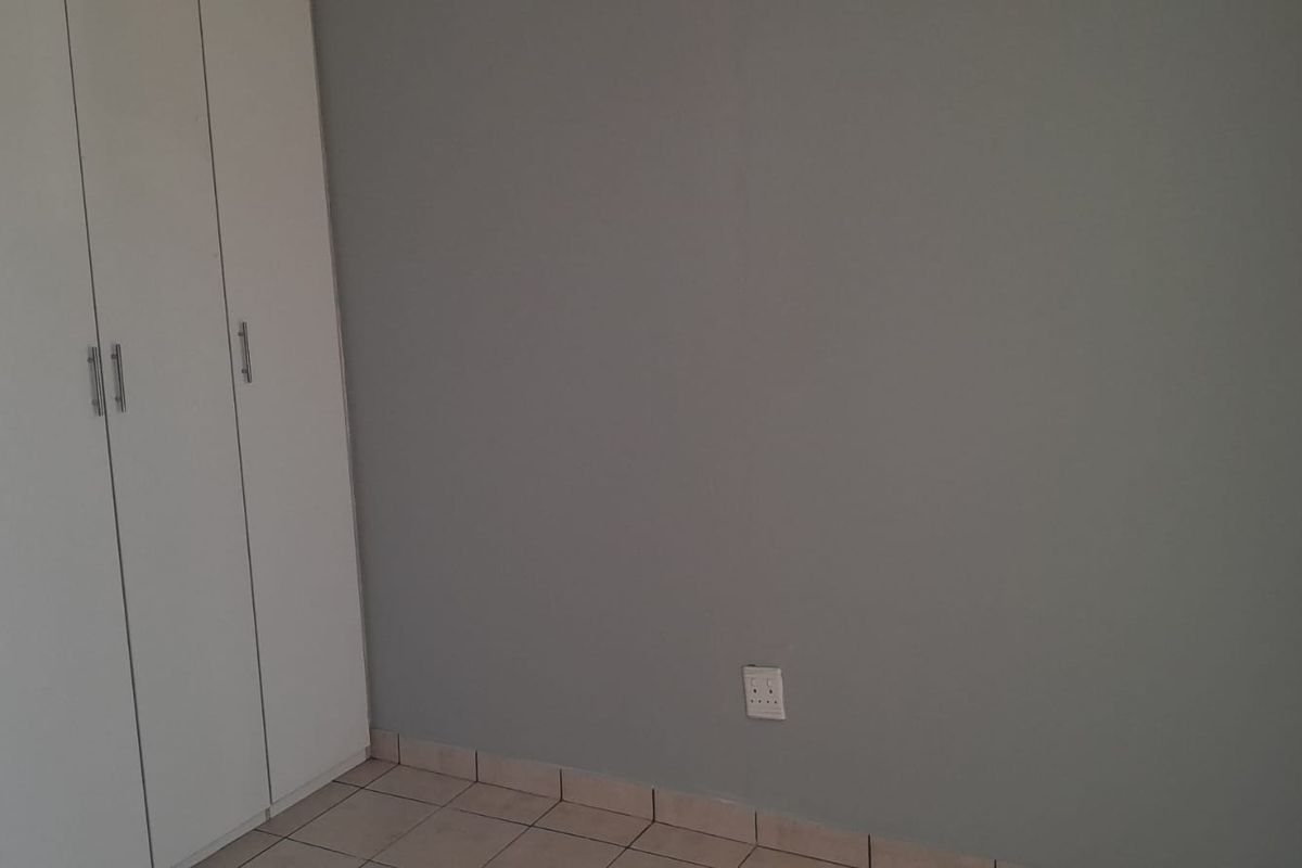 A clean, empty bedroom featuring neutral grey walls, white built-in cupboards, and tiled flooring, providing a versatile space ready for personalization.