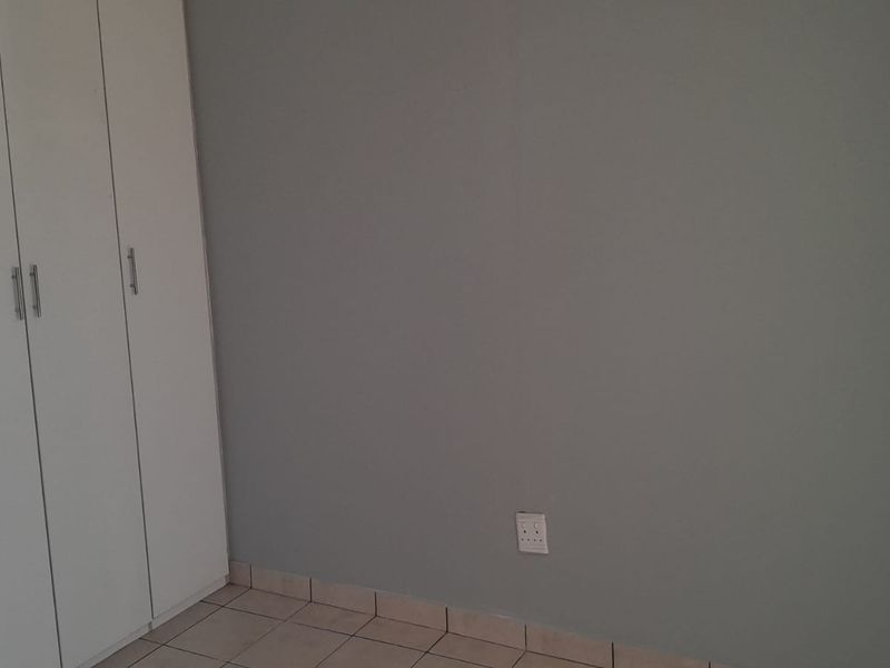 A clean, empty bedroom featuring neutral grey walls, white built-in cupboards, and tiled flooring, providing a versatile space ready for personalization.
