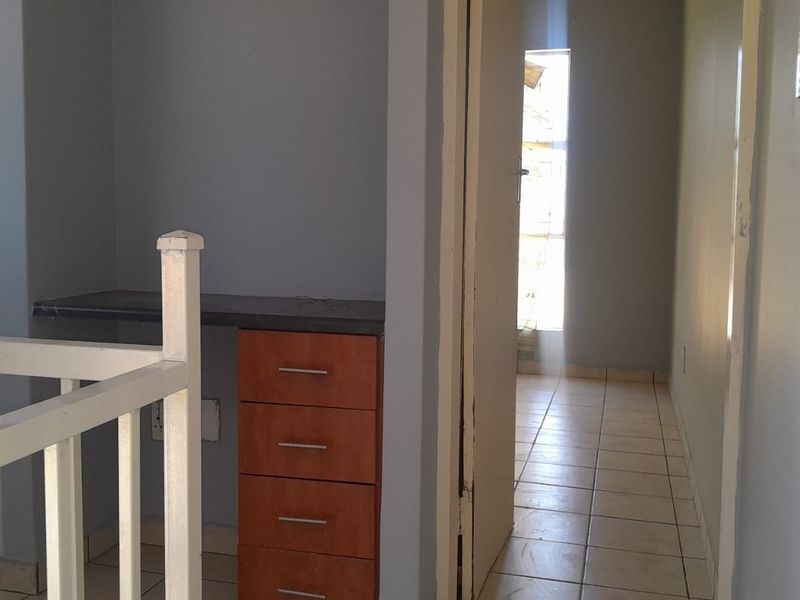 A hallway area featuring a built-in desk with drawers, tiled flooring, and a staircase railing, leading into an adjacent room.