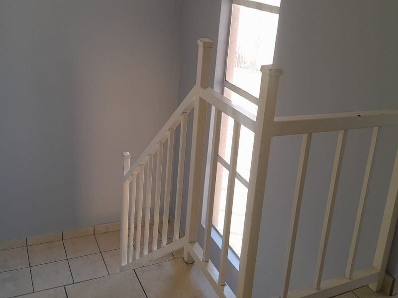A simple interior hallway featuring a staircase with a white balustrade and tiled flooring, providing access between levels.