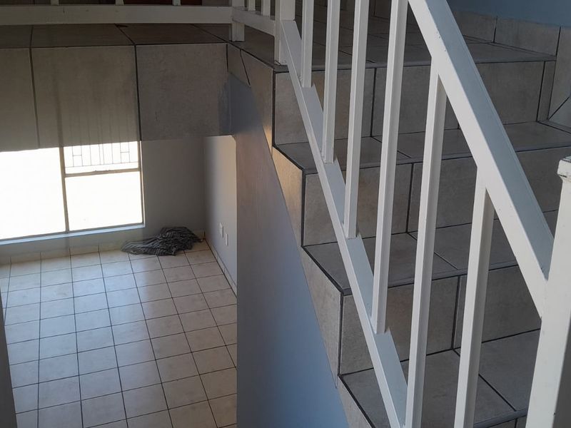 A functional hallway featuring a tiled staircase with a white metal balustrade and neutral floor tiles, leading to an open lower level area.