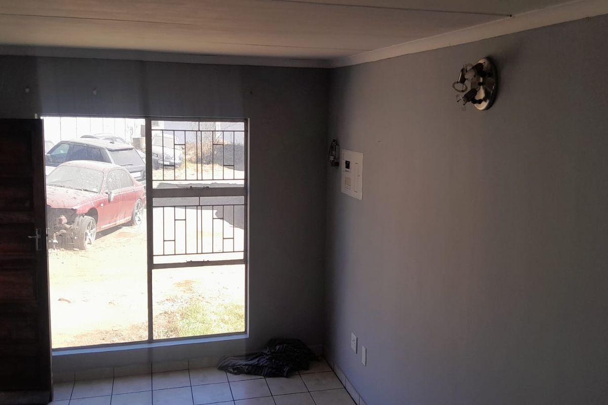 An empty living room featuring tiled flooring, security bars on the window, and an exposed electrical distribution board with a missing light fixture cover.