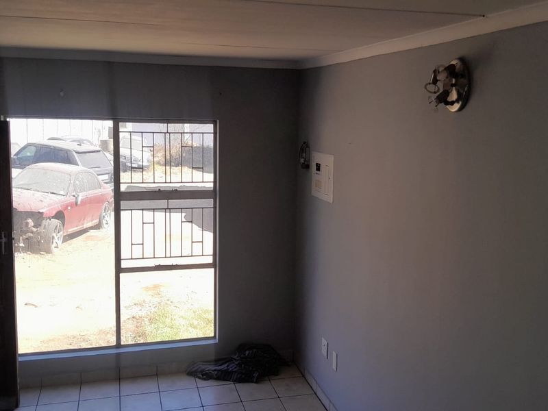 An empty living room featuring tiled flooring, security bars on the window, and an exposed electrical distribution board with a missing light fixture cover.