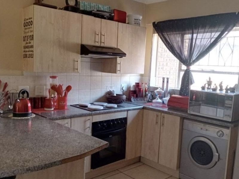 Functional kitchen featuring light wood-finish cabinetry, granite-look countertops, built-in oven with extractor fan, and tiled flooring with integrated laundry appliance space.