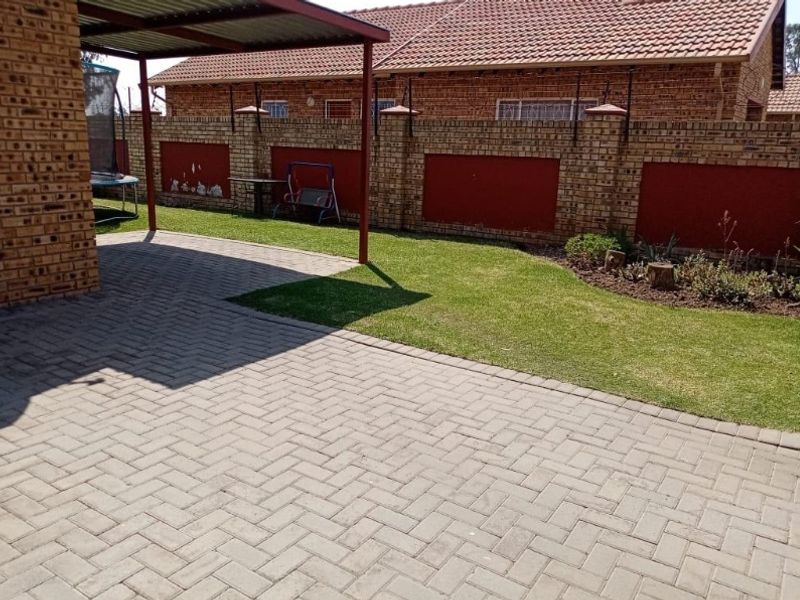 A private rear garden featuring a paved patio area, a covered carport, and a secure brick boundary wall.