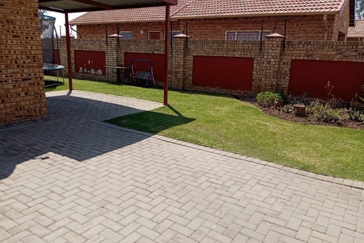 A private rear garden featuring a paved patio area, a covered carport, and a secure brick boundary wall.