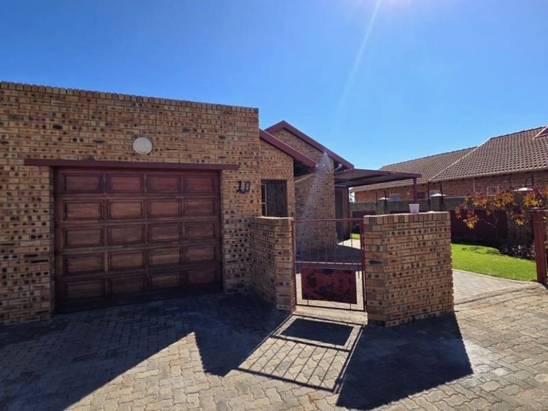 Front exterior view of a face brick apartment unit featuring a paved driveway, sectional garage door, and a gated pedestrian entrance.