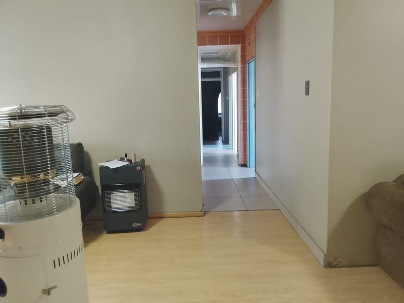 A living area with laminate flooring leading into a tiled hallway, showing signs of wear on the lower wall sections.