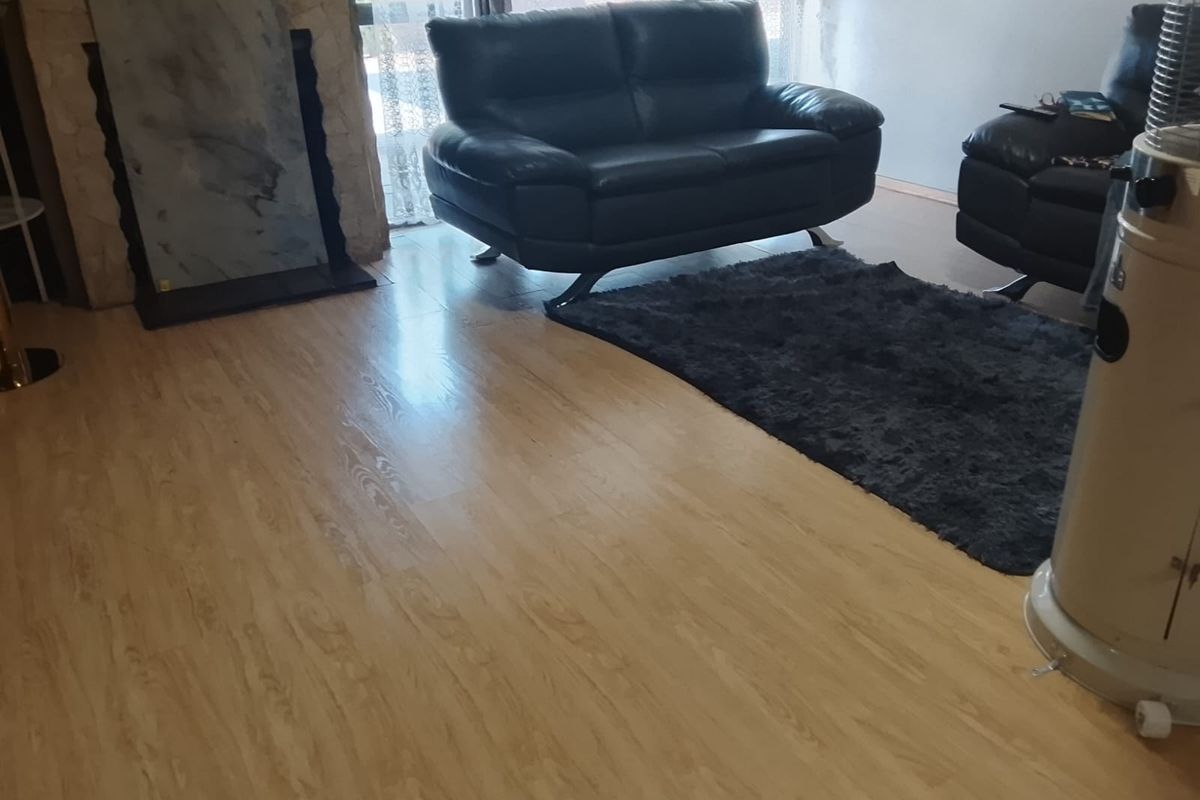 A living room featuring light-toned laminate flooring and a stone-clad fireplace surround.