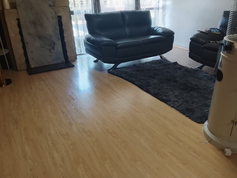 A living room featuring light-toned laminate flooring and a stone-clad fireplace surround.
