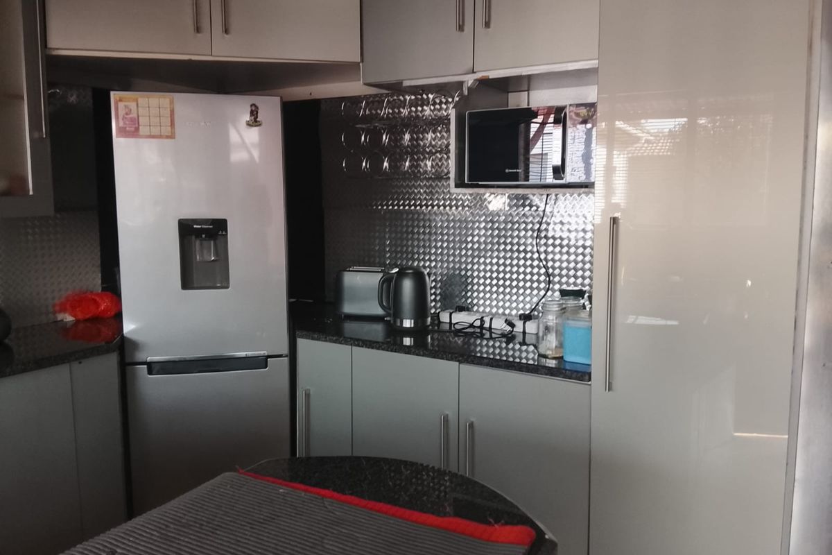 A modern kitchen featuring sleek high-gloss cabinetry, granite countertops, and a distinctive metallic backsplash, providing a functional and contemporary cooking space.