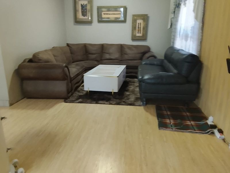 A living room featuring light-toned laminate flooring and a window, providing a functional space for relaxation.