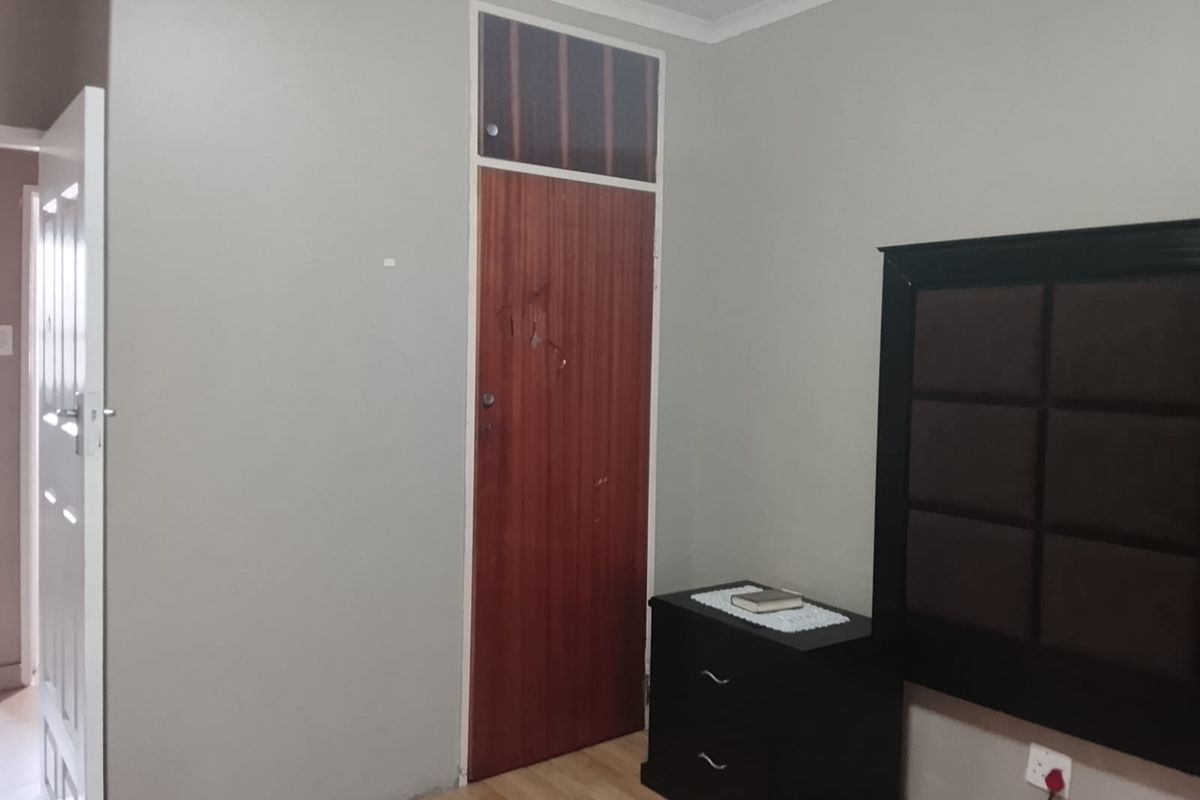A bedroom featuring laminate flooring, a wooden door with a transom window, and neutral wall finishes.