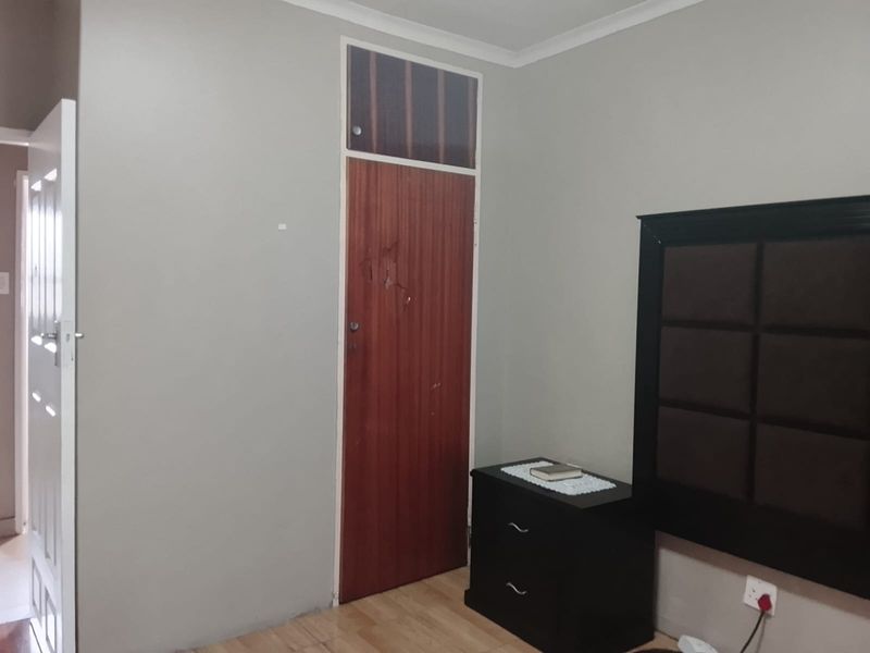 A bedroom featuring laminate flooring, a wooden door with a transom window, and neutral wall finishes.