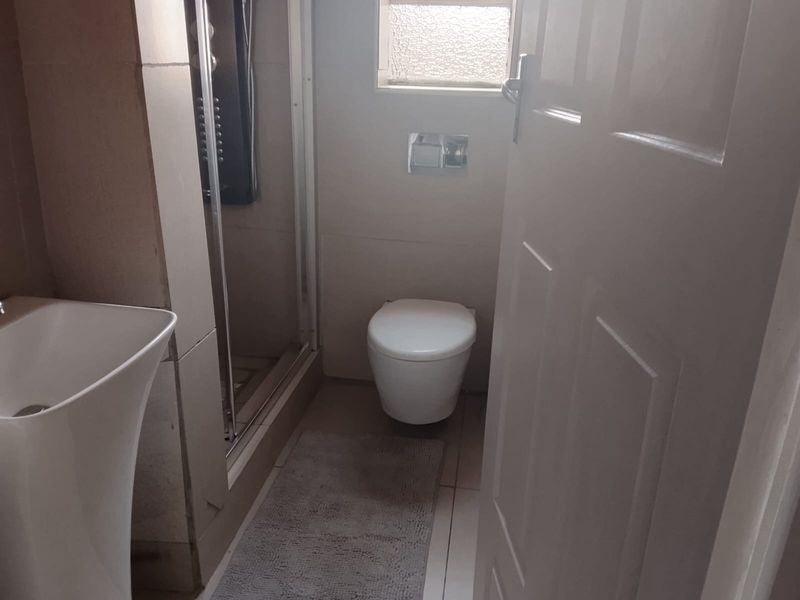 A compact bathroom featuring a wall-mounted toilet, a shower enclosure, and a pedestal basin with tiled finishes throughout.