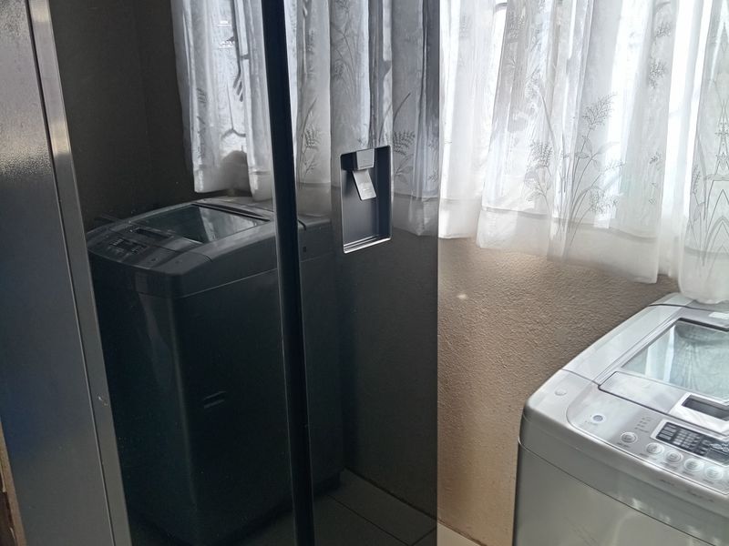 A functional laundry area featuring tiled flooring and a window with security bars, providing a practical space for utility and appliance storage.