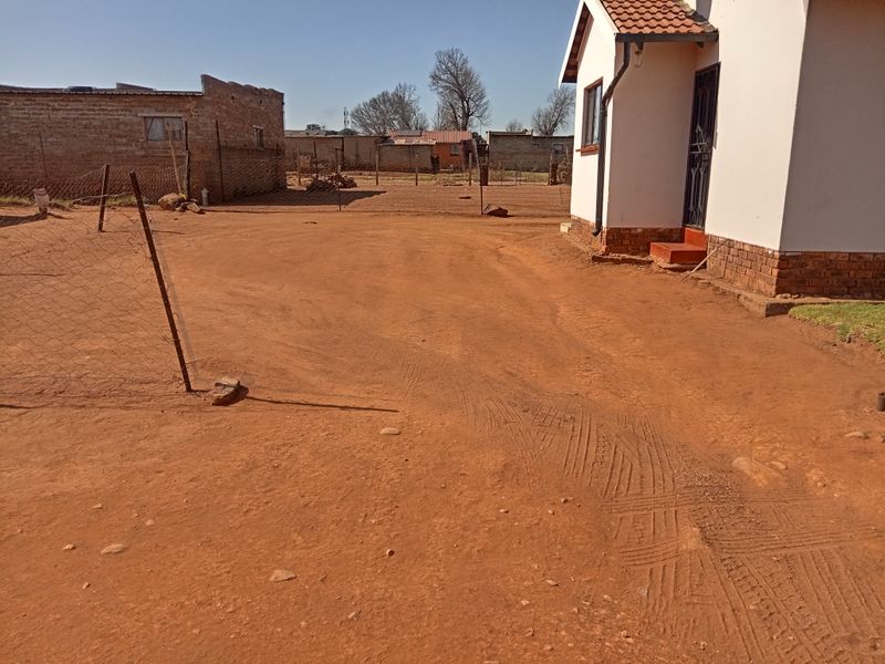 A view of the rear exterior of the house featuring a large unpaved yard area and simple brick and tile construction.