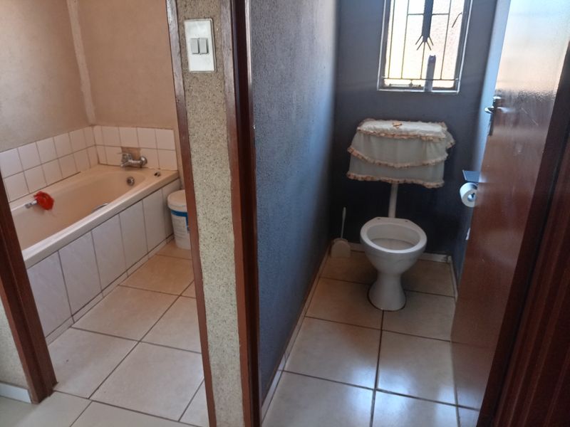 A functional bathroom featuring a separate bathtub area and a private toilet cubicle with tiled flooring and security bars on the window.