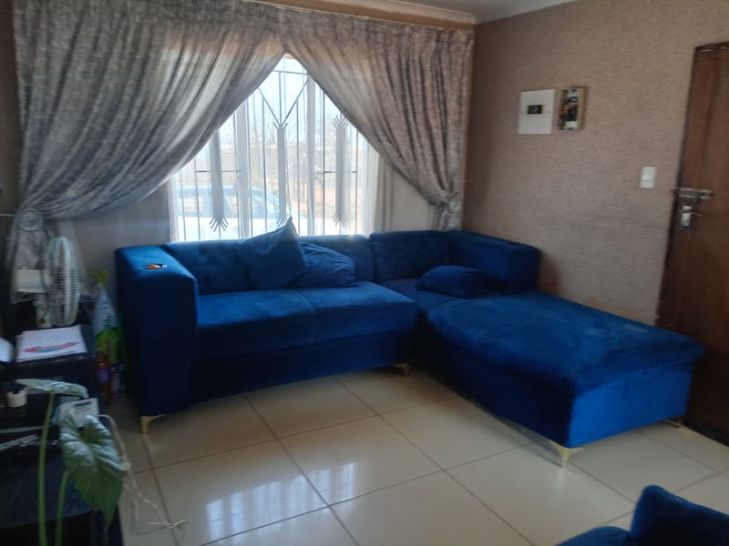 A living room featuring tiled flooring, a window with security bars, and cove cornicing, providing a functional space with potential for cosmetic updates.