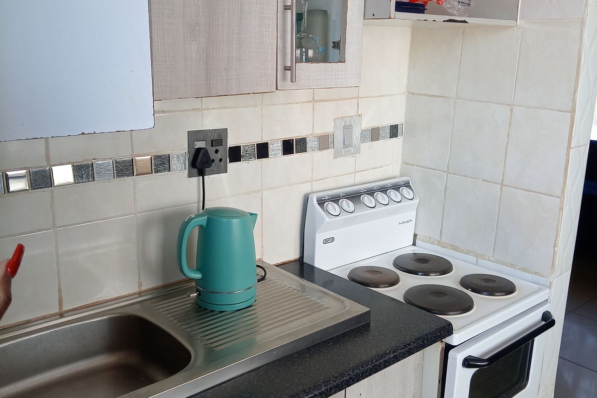 Compact kitchen featuring a stainless steel sink, electric stove, and tiled backsplash with built-in cabinetry requiring some maintenance and cosmetic updates.
