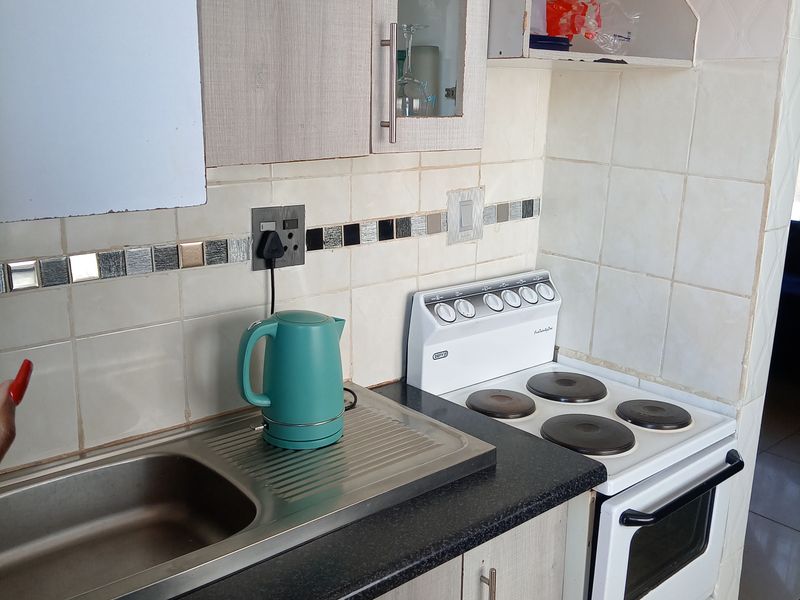 Compact kitchen featuring a stainless steel sink, electric stove, and tiled backsplash with built-in cabinetry requiring some maintenance and cosmetic updates.