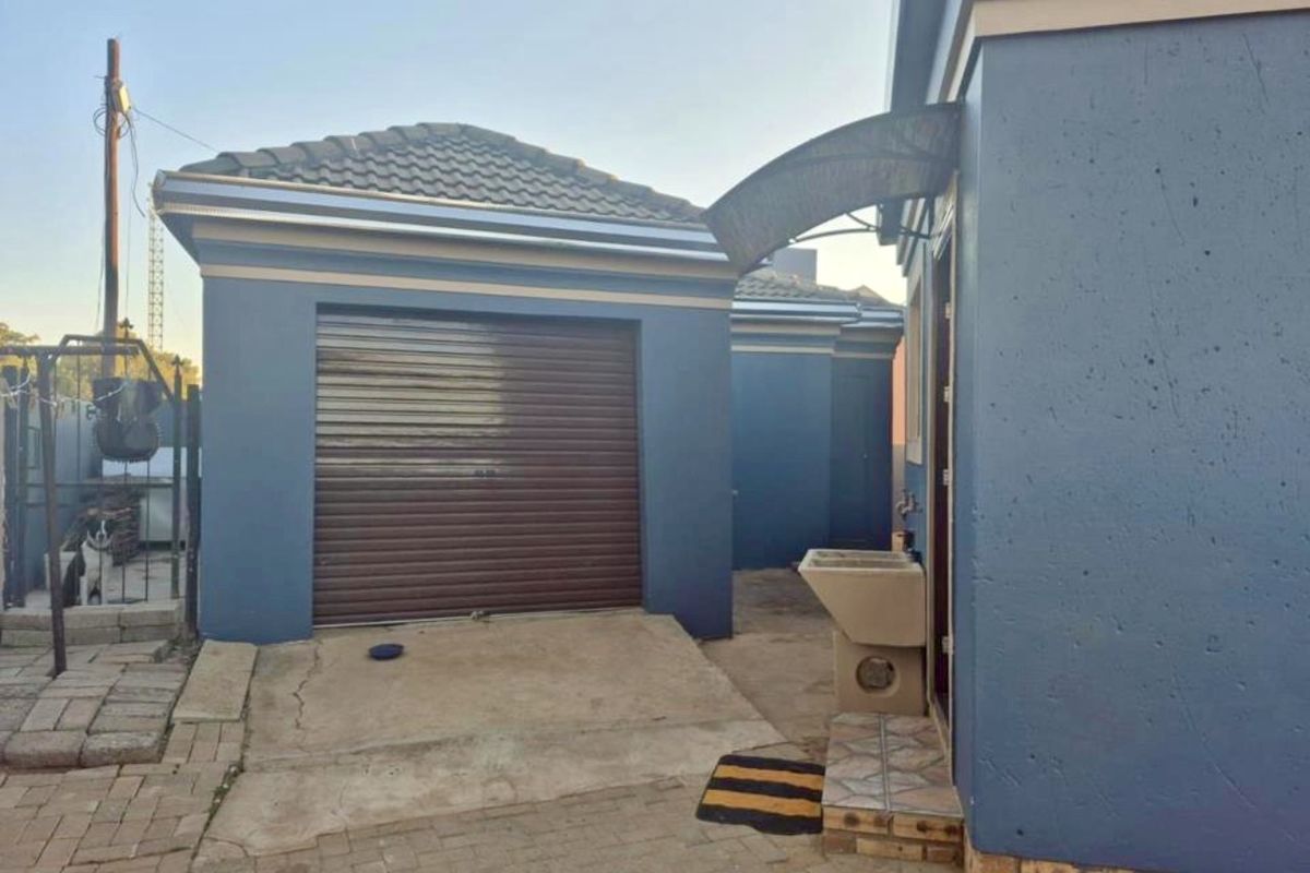 Rear exterior view showing a single garage with a roller door, concrete driveway, and an external utility sink area.