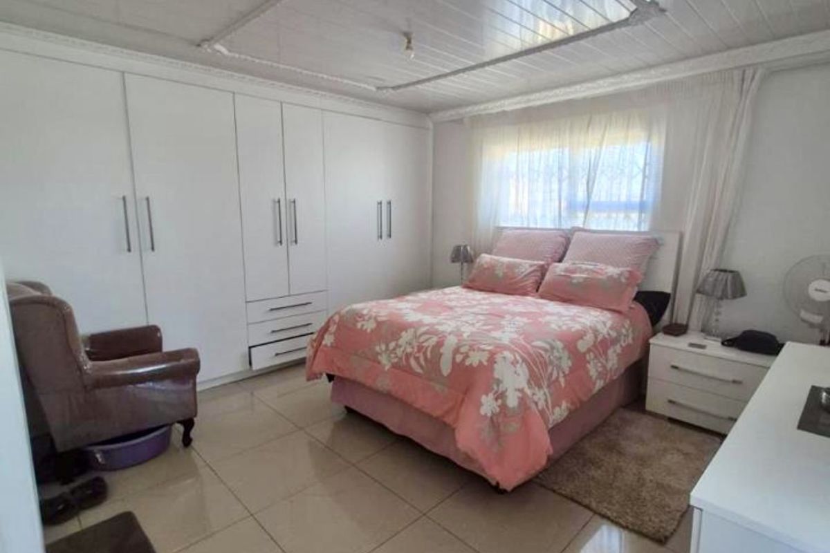 A spacious bedroom featuring large built-in cupboards, neutral tiled flooring, and a white tongue and groove ceiling.