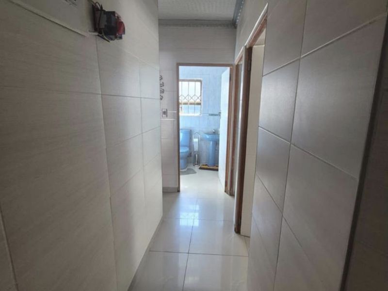 A tiled hallway featuring wall-to-wall tiling and a visible electrical distribution board, leading towards a bathroom area.