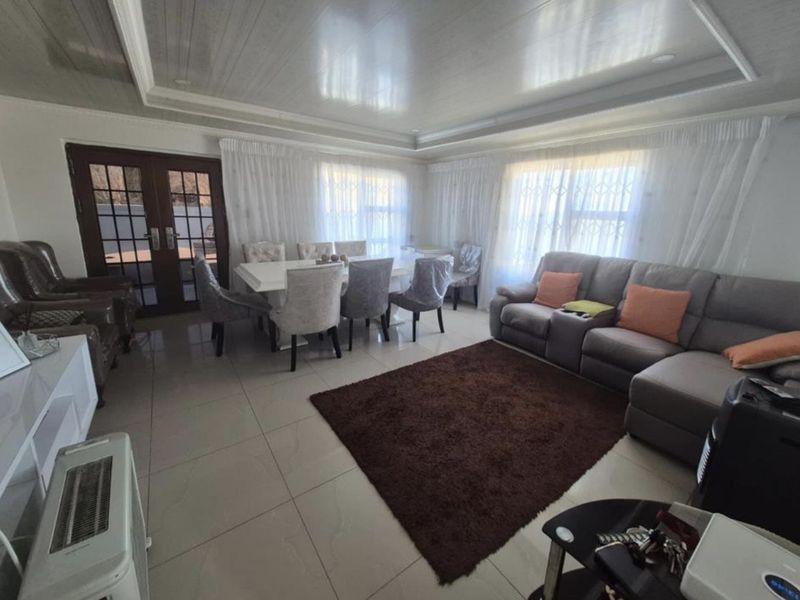 Spacious open-plan living and dining area featuring large format floor tiles, a recessed ceiling design, and double glass doors leading to the exterior.
