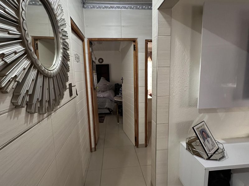 A tiled hallway featuring decorative ceiling cornices and wall tiling, providing access to adjacent rooms within the home.